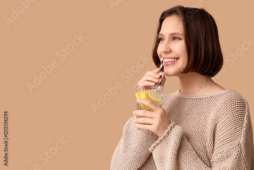 Pretty young woman drinking infused water on beige background photo