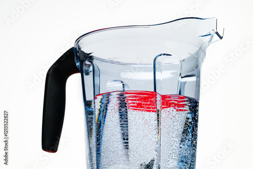 Red surface reflected into bubbly water in a clear plastic blender container against a white backdrop photo