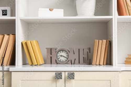 Shelves with books, clock and stylish decor, closeup photo