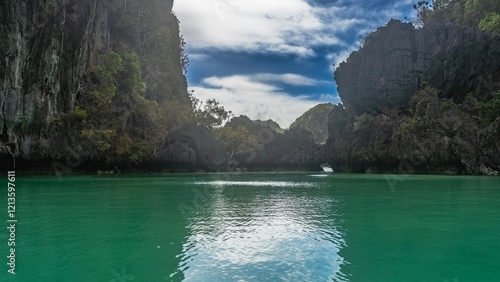 The emerald lagoon is surrounded by sheer karst cliffs. Green tropical vegetation on steep slopes. An arch in the rocks in the distance. Blue sky, clouds. Reflection. Philippines. Palawan.Small lagoon photo