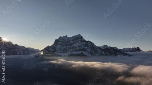 Breathtaking aerial view of Glärnisch and Rautispitz peaks in Glarus Nord, Switzerland, golden sunlight bathes alpine scene, rising above thick cloud blanket. photo