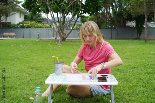 Young woman beading colorful bracelets outdoors in a park photo