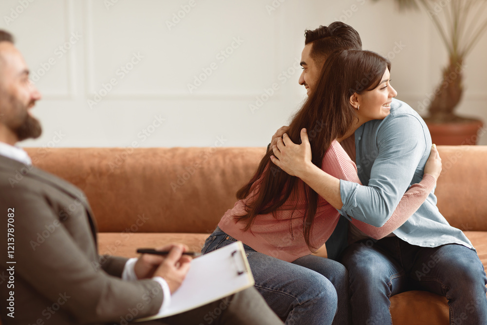 Making Peace. Happy young married couple hugging after successful therapy session with man psychologist, loving spouses reconcile after fight or relationships problems after talk with expert Making Peace. Happy young married couple hugging after successful therapy session with man psychologist, loving spouses reconcile after fight or relationships problems after talk with expert