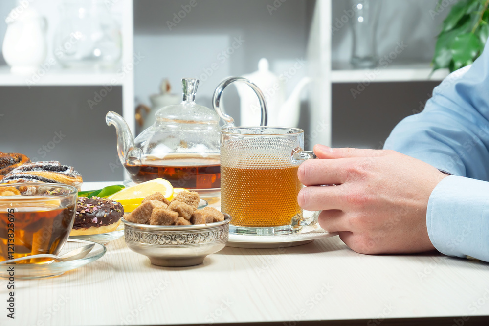 A young man in a blue shirt holds a cup of tea in his hands. He adds sugar to taste and stirs it. Close-up of his hands. A young man in a blue shirt holds a cup of tea in his hands. He adds sugar to taste and stirs it. Close-up of his hands.