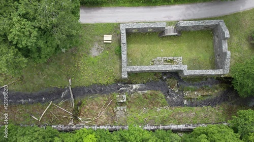 Top-down aerial view of stone ruins and a flowing stream surrounded by greenery at Bäckefors Bruk, Sweden photo