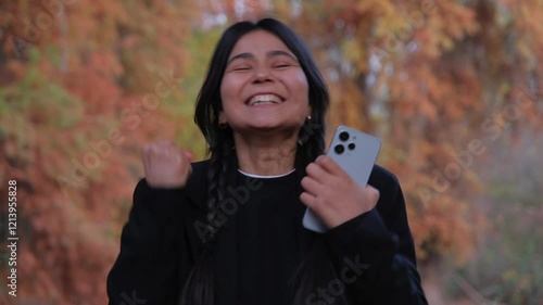 Happy woman holding a phone, reacting to a lucky surprise with amazement and celebration. Ideal for themes of triumph, positivity, and joyful achievements. Perfect for conveying good news and success