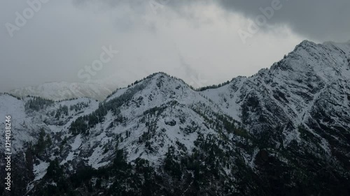 Snow-dusted rocky cliffs rising against a backdrop of misty, snow-covered mountains. 
 photo