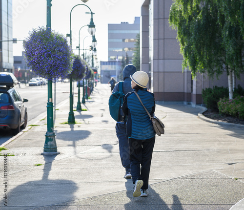 Tourists walking on the  pedestrian sidewalk at downtown Anchorage. Purple flower baskets hanging from the lamp posts. Alaska.