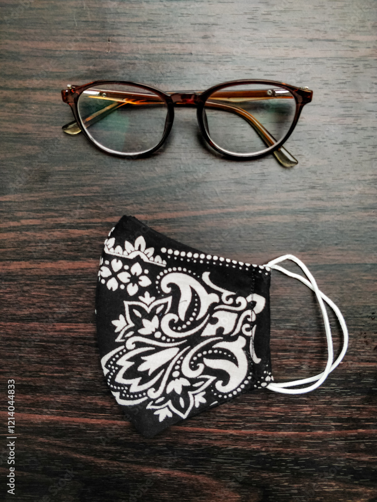 Stylish glasses and a handmade floral mask placed on a dark wooden table, creating an appealing contrast.