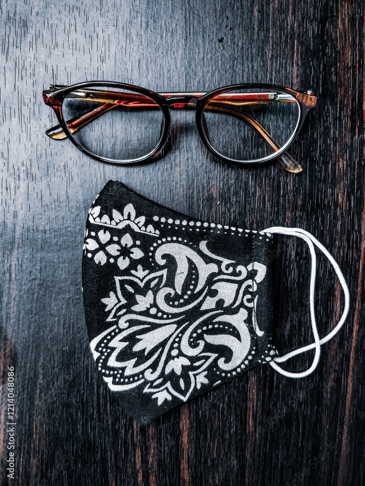 Stylish glasses and a handmade floral mask placed on a dark wooden table, creating an appealing contrast.