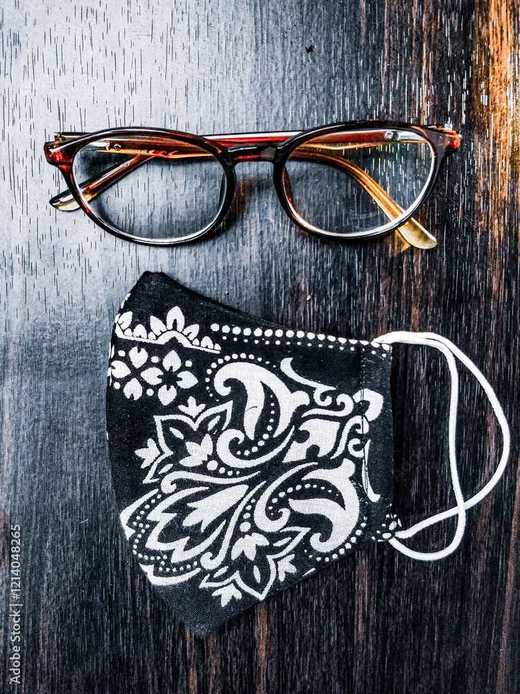 Stylish glasses and a handmade floral mask placed on a dark wooden table, creating an appealing contrast.