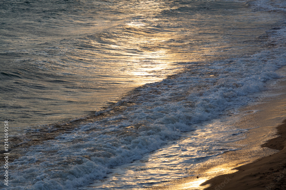 Golden sunset reflecting on gentle waves reaching sandy beach