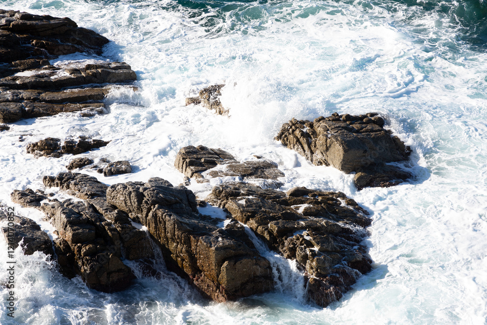 Ocean waves crashing on rocks in a sunny day
