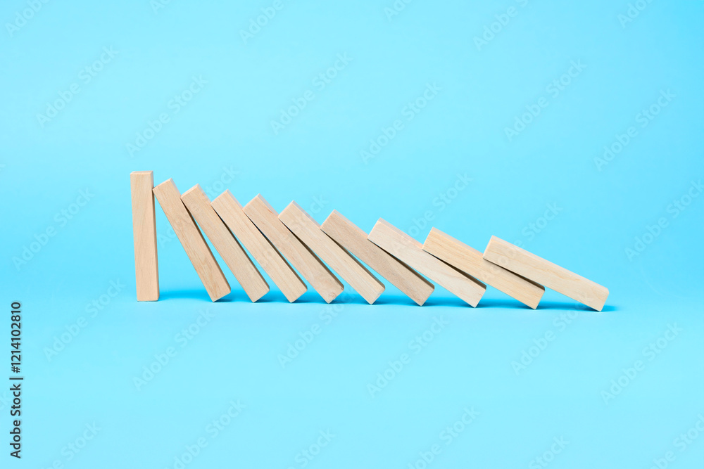 Domino effect. Wooden blocks falling on light blue background. Space for text Domino effect. Wooden blocks falling on light blue background. Space for text