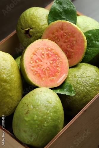 Fresh cut and whole guava fruits in wooden crate on table, closeup