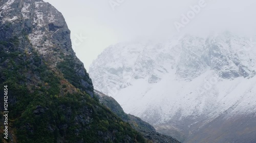 Snow-dusted rocky cliffs rising against a backdrop of misty, snow-covered mountains. The composition highlights the rugged beauty and serene atmosphere of the alpine landscape. photo