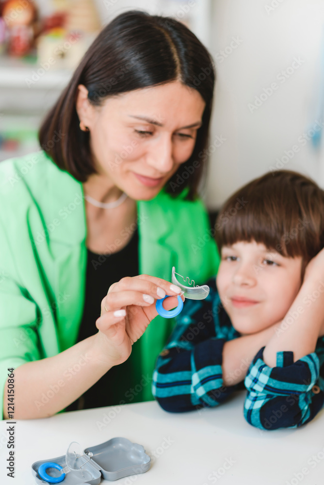 A female speech therapist shows a boy an orthodontic plate to correct his bite. A female speech therapist shows a boy an orthodontic plate to correct his bite.
