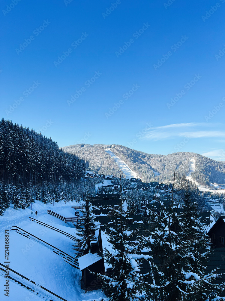 Fototapeta premium Snowy mountain village surrounded by scenic forest and clear blue sky