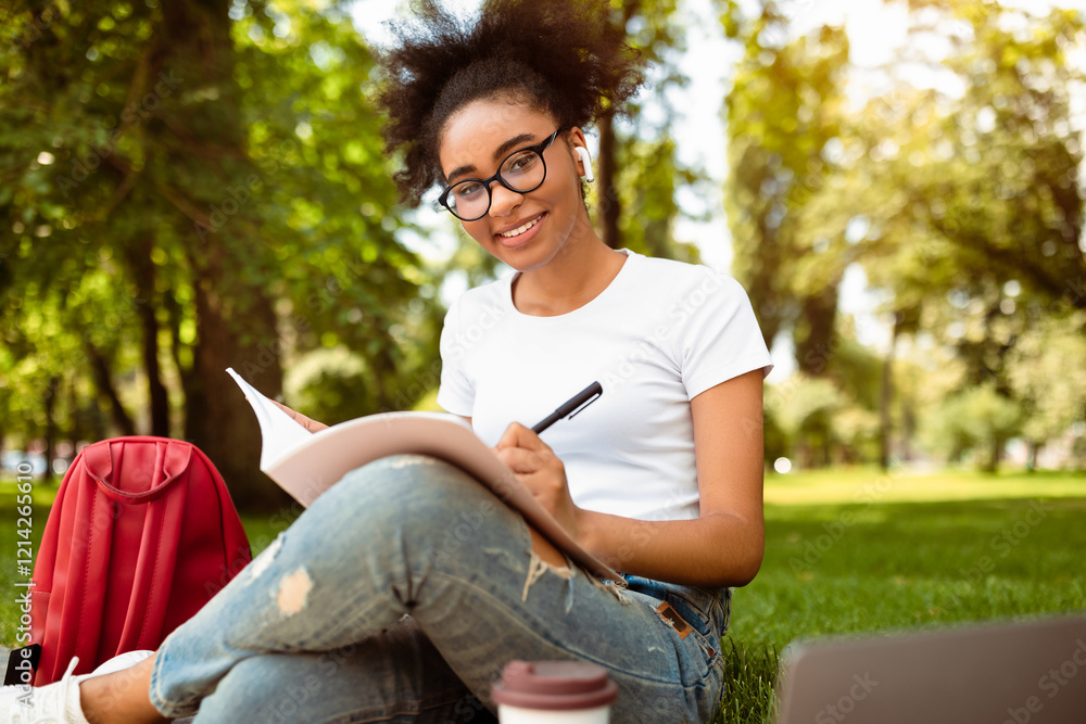 Obraz premium Cheerful Black College Girl Taking Notes Learning Sitting In Park Outdoor. Studentship And Modern Education Concept. Successful African American Student Preparing Homework.