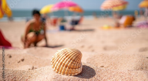 Seashell in focus on sandy beach with blurred figures and umbrellas in background photo