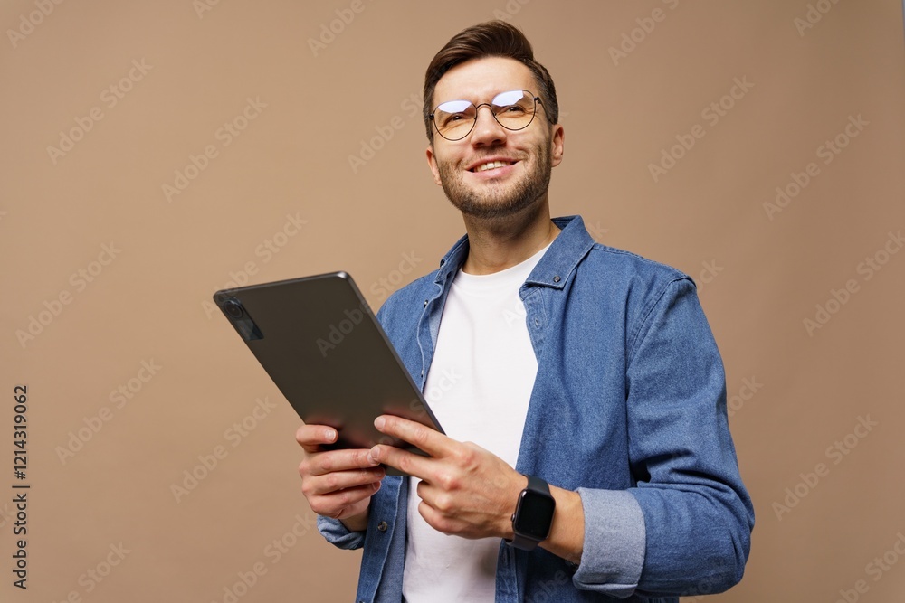 Young man in glasses holds tablet while smiling against a neutral background Young man in glasses holds tablet while smiling against a neutral background