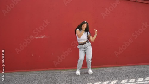 Full length video of an asian young female energetic dancer performing K-pop urban dance in the city against a red wall