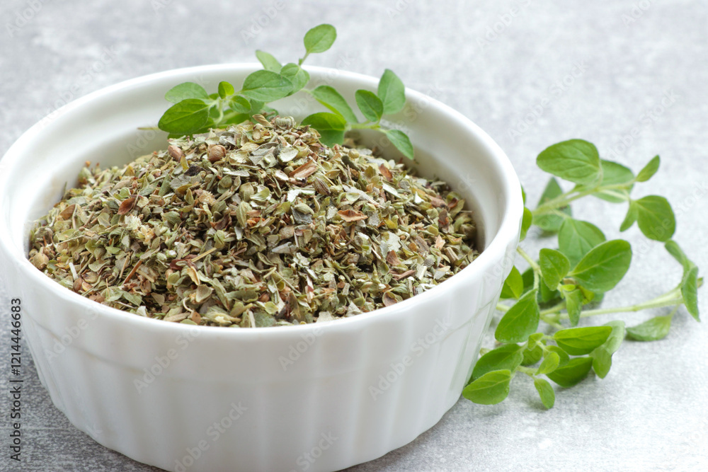 Dried oregano in bowl and green leaves on light grey table, closeup Dried oregano in bowl and green leaves on light grey table, closeup
