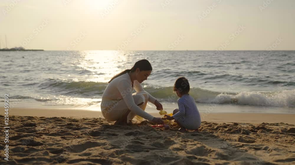 happy toddler baby girl playing sand toy with mother on the sea beach at sunset in Pattaya, Thailand happy toddler baby girl playing sand toy with mother on the sea beach at sunset in Pattaya, Thailand