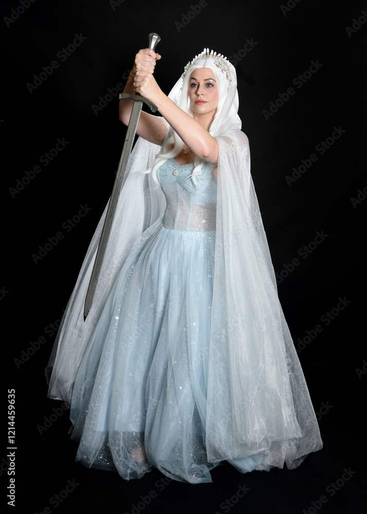 Fototapeta premium full length portrait beautiful blonde fantasy maiden faery wearing medieval fairytale ballgown costume, flowing white hooded cape. standing pose holding a sword weapon, isolated dark studio background