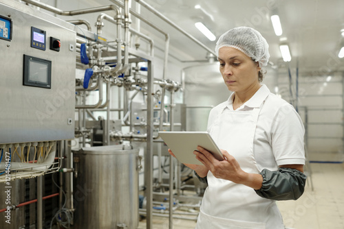 Tapeta Engineer inspecting machinery in sterile industrial facility while holding digital tablet