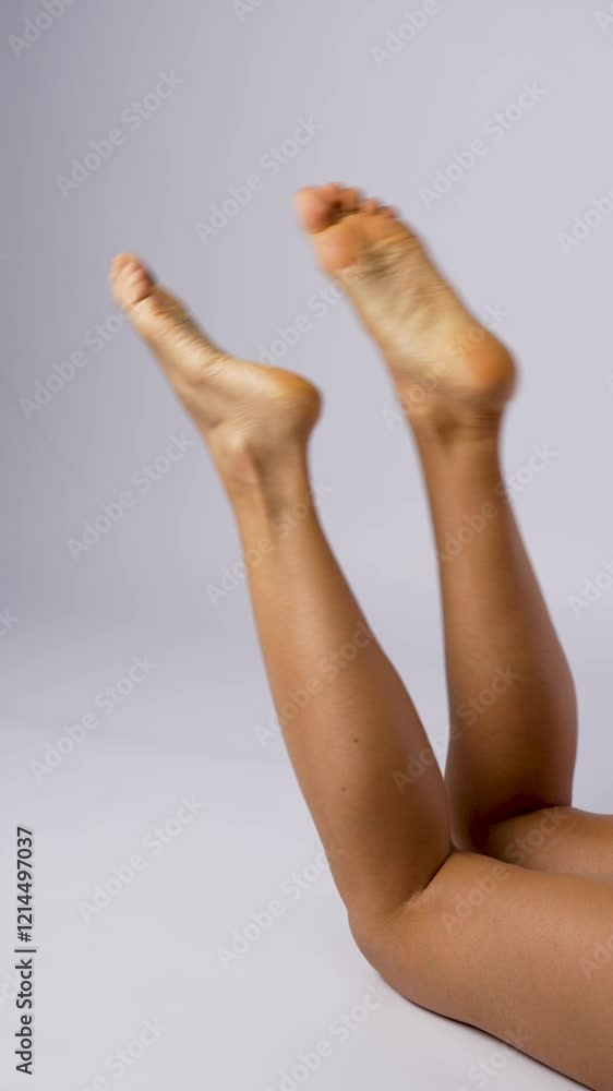 Young woman shaking her legs. Close-up of female barefoot legs lying on white background, vertical Young woman shaking her legs. Close-up of female barefoot legs lying on white background, vertical