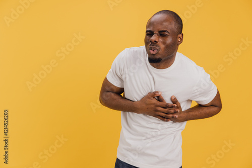 Young man suffering chest pain on yellow background photo