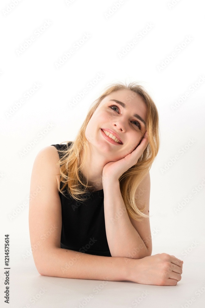 Young woman with blonde hair smiling while resting her chin on her hand in a bright studio setting Young woman with blonde hair smiling while resting her chin on her hand in a bright studio setting