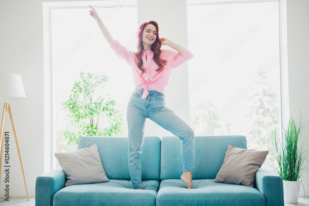 Full size photo of pretty young woman dance point finger headphones couch modern bright interior apartment indoors Full size photo of pretty young woman dance point finger headphones couch modern bright interior apartment indoors