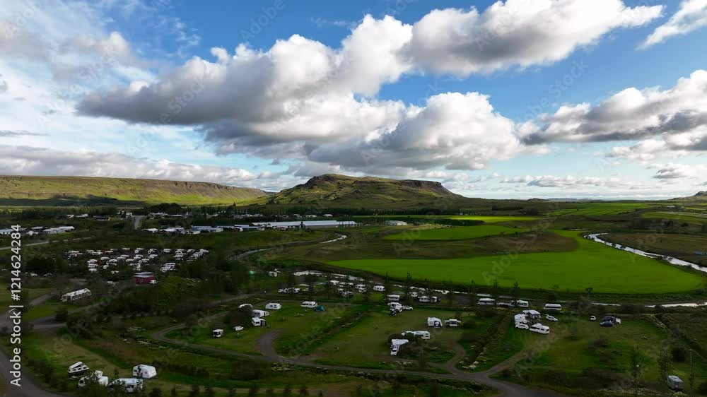 A drone flies over a trailer campsite nestled in green meadows and surrounded by majestic mountains. The stunning scenery captures the peaceful beauty of the camping area amid the breathtaking Iceland A drone flies over a trailer campsite nestled in green meadows and surrounded by majestic mountains. The stunning scenery captures the peaceful beauty of the camping area amid the breathtaking Iceland