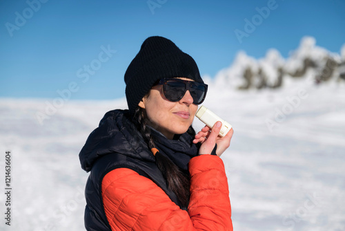 Young woman applying sunscreen stick  in the winter mountain .Spf stick 