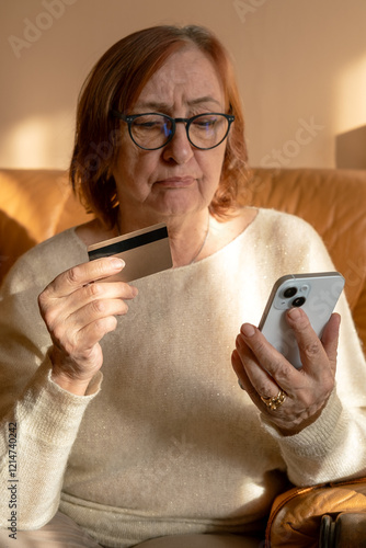 Old 70s woman, senior granny, elderly lady, retired grandmother with mobile phone and bank credit card paying online shopping with smartphone, buying at home. 
