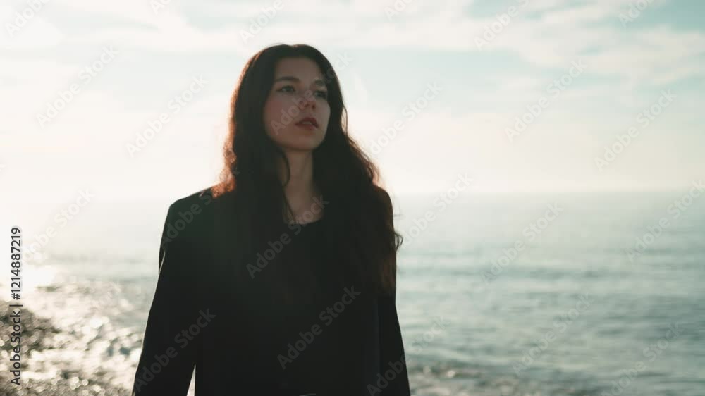 Woman wearing black jacket walking rocky coastline during slow motion, revealing contemplative journey near dramatic seascape with crashing ocean waves Woman wearing black jacket walking rocky coastline during slow motion, revealing contemplative journey near dramatic seascape with crashing ocean waves