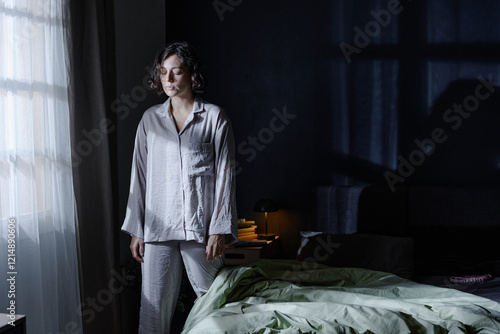 Wide shot of woman with closed eyes dressed in pajamas standing near window silently in bedroom