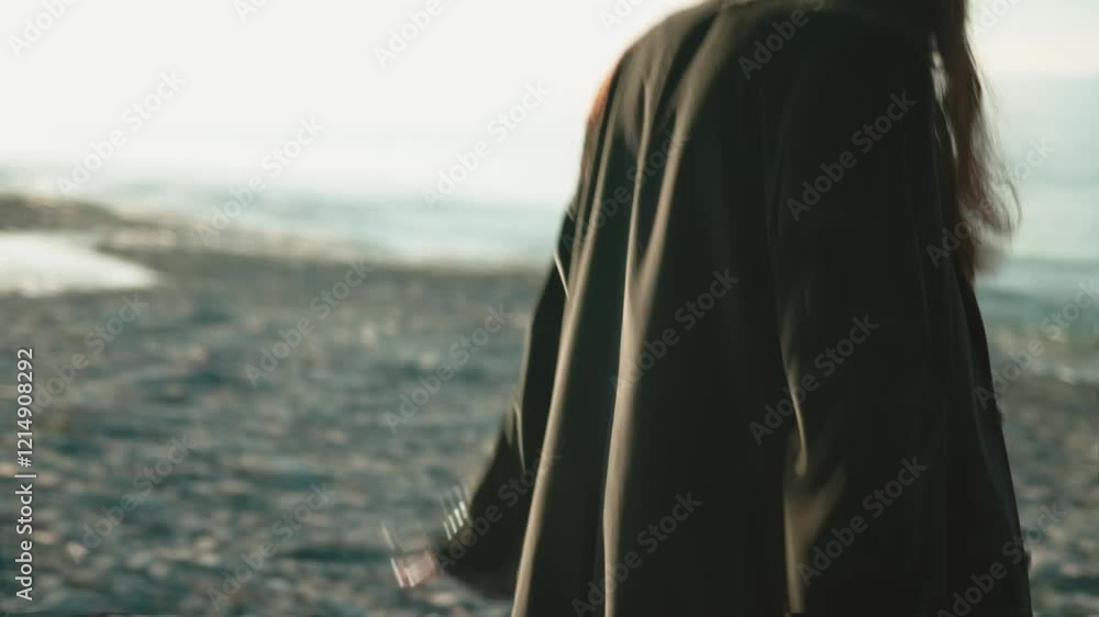 Beautiful young woman with long brown hair wearing a black jacket and gray trousers walks on a pebble beach near the ocean, enjoying the fresh air and freedom in slow motion Beautiful young woman with long brown hair wearing a black jacket and gray trousers walks on a pebble beach near the ocean, enjoying the fresh air and freedom in slow motion