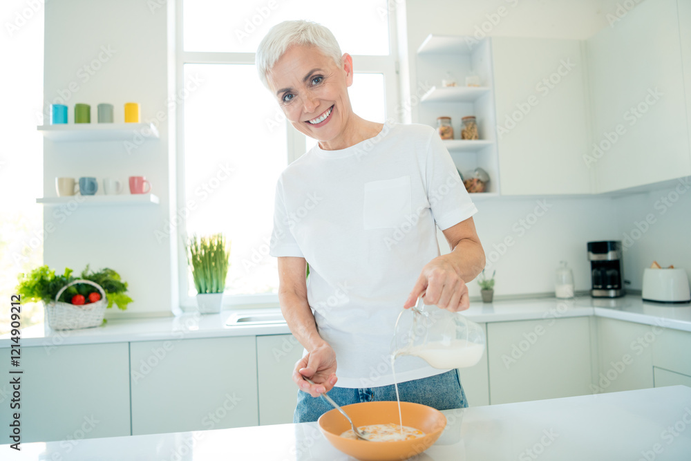 Charming mature woman pours milk over cereal in bright modern kitchen during a sunny day, showcasing happiness and culinary skills. Charming mature woman pours milk over cereal in bright modern kitchen during a sunny day, showcasing happiness and culinary skills.