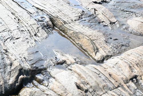 Water has collected on the rock's surface. The rock is a brown color and smooth. In hilly areas, during monsoon season, rain water gets collected in these rocks. Small water pond on top of the rock.