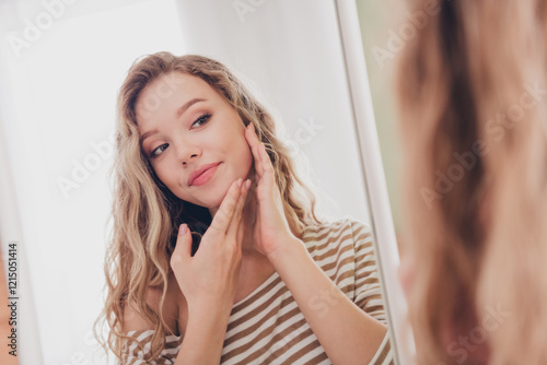 Fotografi Charming young woman with blond hair gazing at herself in mirror, reflecting self-care and happiness, dressed in a striped pullover, enjoying leisure time indoors in a cozy living room setting