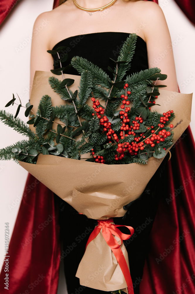 Portrait of a woman in a studio with professional lighting in a black elegant dress with a Christmas tree bouquet against the background of a large red bow