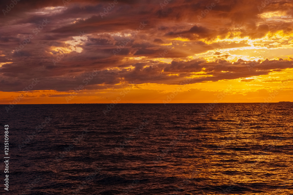 Fototapeta premium the water surface of the sea under a cloudy sky, illuminated by the rays of the setting sun at sunset