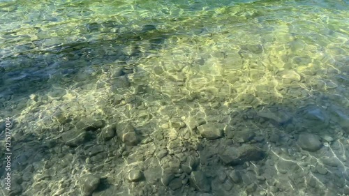 Klares durchsichtiges im Sonnenschein schimmernde Wasseroberfläche. Steiniger Untergrund.