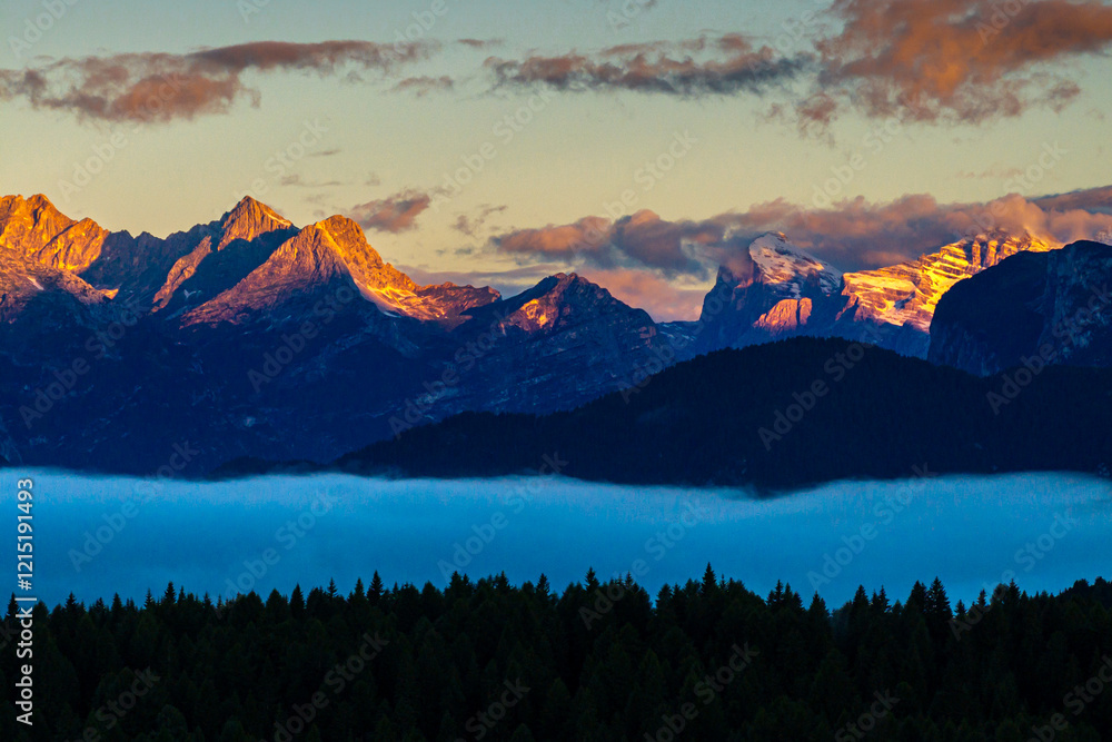 Sunrise aerial photo over the Dolomites with vibrant hues on the Antelao and Cridola peaks, framed by dense alpine forests below. Captured near Danta village, Italy. Hiking in Italy.