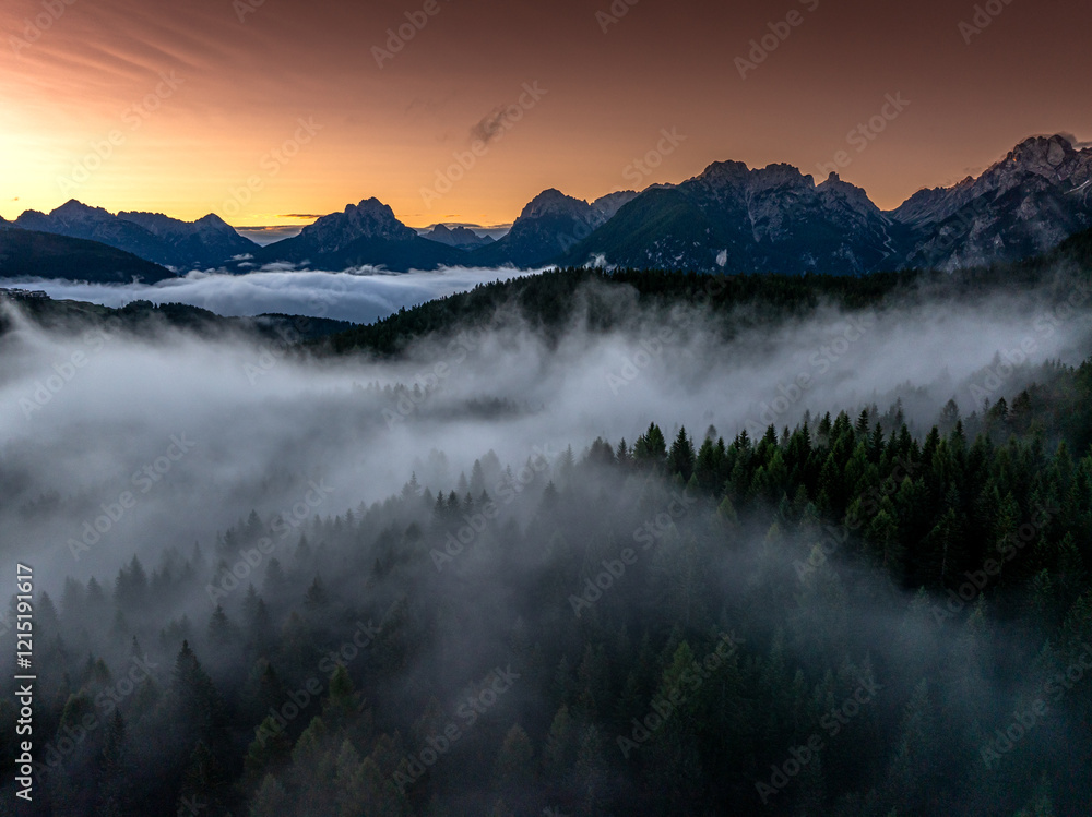 Sunrise aerial photo over the Dolomites with vibrant hues on the Antelao and Cridola peaks, framed by dense alpine forests below. Captured near Danta village, Italy. Hiking in Italy.