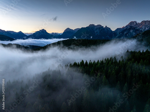 Obraz na płótnie A mist-filled valley in the Dolomites at sunrise, with sunlight highlighting the peaks and dense alpine forest below. Taken near Danta village, Italy. Aerial photo with Dolomites. Hike in Italy. w salonie