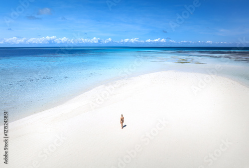 Aerial view of alone young woman on the sandbank in ocean, white sand, blue sea during low tide at sunny summer day in Nakupenda, Zanzibar island. Top view of girl, sand spit, water, sky with clouds